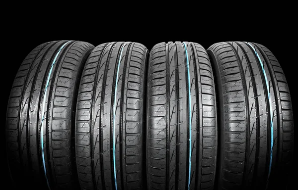 Studio shot of a set of summer car tires on black background. Tire stack background. Car tyre protector close up. Black rubber tire. Brand new car tires. Close up black tyre profile. Car tires in a row