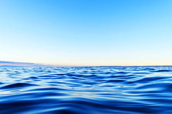 Superficie del agua. Vista de un fondo de cielo al atardecer. Dramático cielo dorado al atardecer con nubes de cielo nocturno sobre el mar. Vista de una textura cristalina del agua de mar. Paisaje. Pequeñas olas. Reflexión del agua — Foto de Stock