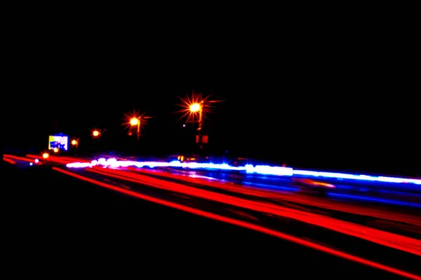 Coches senderos ligeros en una carretera curva por la noche. Rutas de tráfico nocturno. Desenfoque de movimiento. Calle de la ciudad nocturna con movimiento de los faros. Paisaje urbano. Iluminar carretera por vehículo desenfoque de movimiento . — Foto de Stock