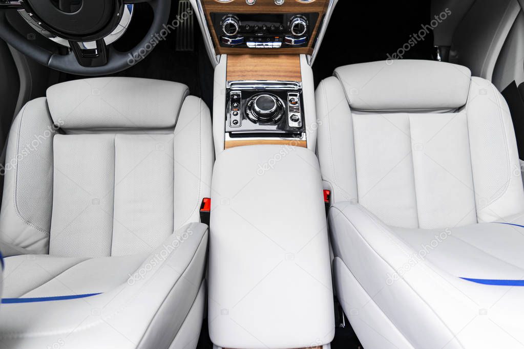 Modern luxury car white leather interior with natural wood panel. Part of leather car seat details with stitching. Interior of prestige modern car. White perforated leather. Car detailing. Car inside