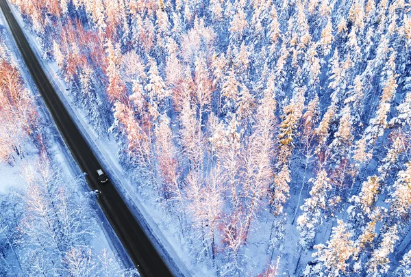 Aerial view of a car on winter road in the forest. Winter landscape countryside. Aerial photography of snowy forest with a car on the road. Captured from above with a drone. Aerial photo. Car in motion