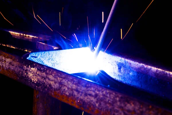 Svetsare Worker utför Jump svetsning. Man svetsare i skyddshandskar utför bågsvetsning process av metallkonstruktioner. Flygande gnistor från svetsmaskinen. Bakgrund byggarbetsplats — Stockfoto