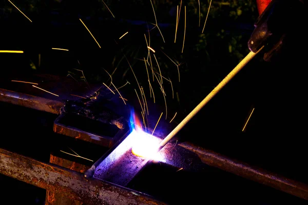 焊工工人执行跳跃焊接。戴防护手套的人类焊工对金属结构进行电弧焊接过程。从焊接机飞溅火花。背景施工现场 — 图库照片