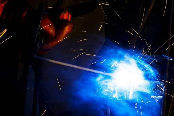 焊工工人执行跳跃焊接。戴防护手套的人类焊工对金属结构进行电弧焊接过程。从焊接机飞溅火花。背景施工现场 — 图库照片