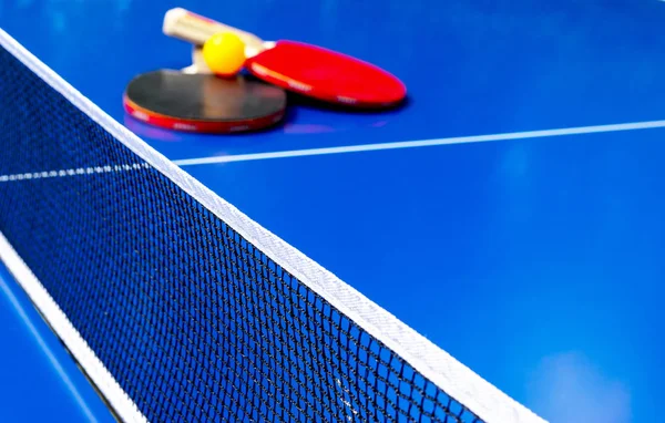 Tennis de table bleu ou ping-pong. Filet de ping-pong en gros plan. Fermez le filet et la ligne de ping-pong. Deux raquettes ou raquettes de ping-pong ou de ping-pong et une balle sur une table bleue avec fond net — Photo