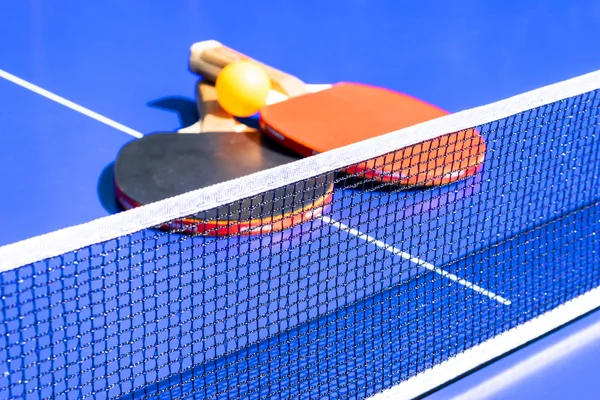 Blue table tennis or ping pong. Close-up ping-pong net. Close up ping pong net and line. Two table tennis or ping pong rackets or paddles  and ball on a blue table with net background