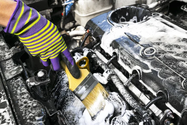 A man cleaning car engine with shampoo and brush. Car detailing or valeting concept. Selective focus. Car detailing. Cleaning with sponge. Worker cleaning. Car wash concept solution to clean