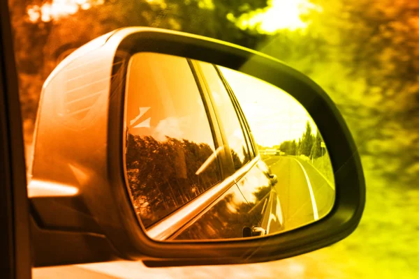 Lonely road seen through rear side mirror. Sky and trees landscape Reflect in Mirror of Car During the Car Moving concept. Travel in summer season. Landscape in the side mirror