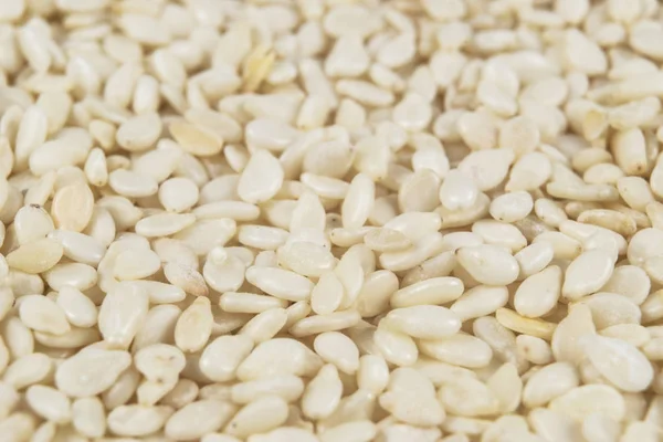 Macro shot de um fundo de semente de sésamo branco cru. Vista superior. Contexto da comida. Um espalhamento de sementes de sésamo. Comida saudável. Alimentos naturais . — Fotografia de Stock
