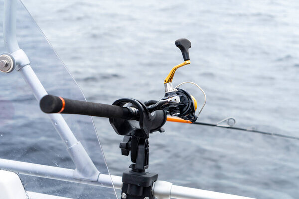 Fishing rod spinning with the line close-up. Fishing rod in rod holder in fishing boat. Fishing rod rings. Fishing tackle. Fishing spinning reel.