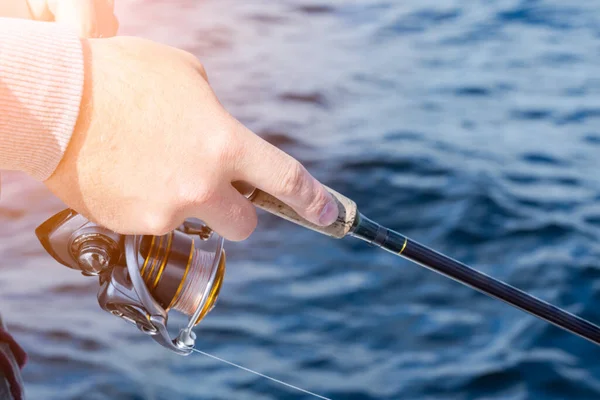 Fishing on the lake. Hands of fisherman with fishing rod and reel. Macro shot. Fishing rod and hands of fisherman over lake water. Spinning rod. Fishing tackle