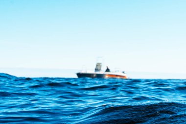 Mavi okyanustaki teknede bulanık bir balıkçıyla su yüzeyi. Bulanık balıkçı teknesiyle güzel bir deniz manzarası. Balıkçı teknesiyle balıkçı teknesi. Okyanus suyu dalgası yansımaları.