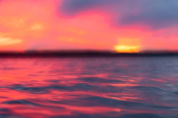 Blurred sunset sky background. Defocused dramatic gold sunset sky clouds over the sea. Blur clear sea water texture. Bokeh light landscape. Small waves. Water reflection