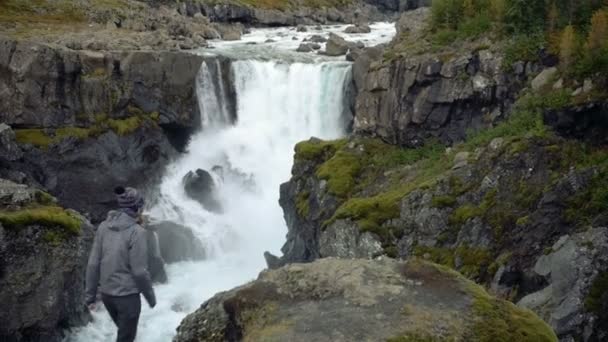 滝の麓の岩の上に立つ女が腕を天に上げ ストック映像