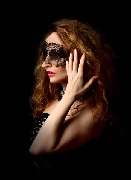 Жінка вирівнює волосся в мереживній масці на чорному фоні — стокове фото