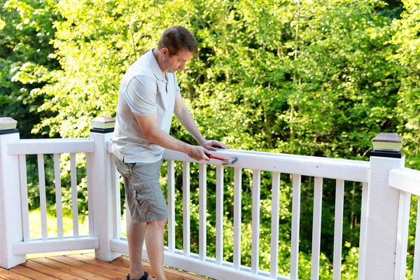 Mature man hammering nail into white railing of outdoor deck — Stock Photo, Image