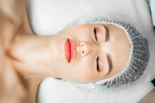 Косметолог-врач делает омолаживающую процедуру для уплотнения и разглаживания морщин на коже лица красивой молодой женщины в салоне красоты — стоковое фото