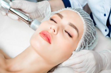 Doktor kozmetik uzmanı, güzellik salonundaki genç ve güzel bir kadının cildindeki kırışıklıkları sıkmak ve düzleştirmek için canlandırıcı yüz enjeksiyonu prosedürünü uyguluyor.