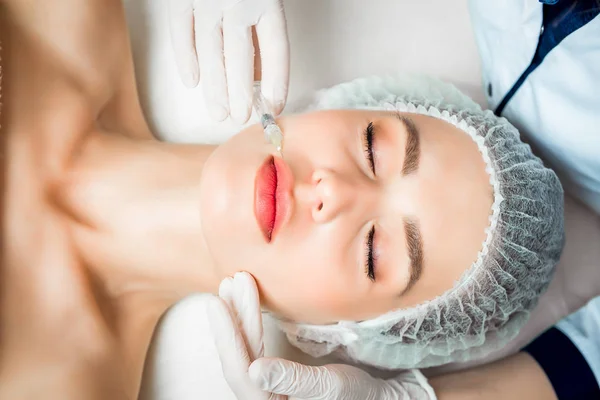 Косметолог-врач делает омолаживающую процедуру для уплотнения и разглаживания морщин на коже лица красивой молодой женщины в салоне красоты Лицензионные Стоковые Фото