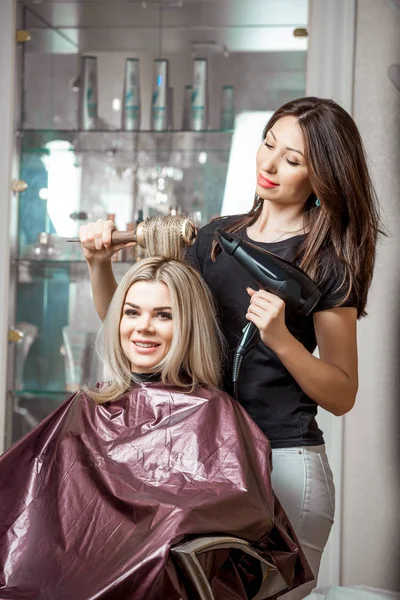 Stilvolle professionelle Friseurin, die dem Kunden mit einem Haartrockner auf dem Hintergrund des Friseursalons frisiert — Stockfoto