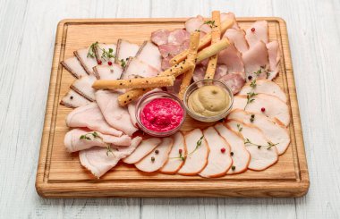 Et ve ahşap bir tahtanın üzerinde soslu ve ekmek çubuklu çeşitli sosisler.