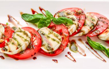 Beyaz tabakta mozzarella, domates, fesleğen ve balzamik sirkeli Caprese salatası. Ahşap arka planda