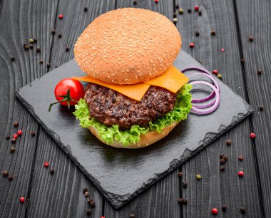 Salata ve peynirli ev yapımı burger. Siyah tahta üzerine serilmiş.