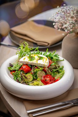 Peynirli vejetaryen salatası. Marul, domates, salatalık ve peynirli renkli salata dekorlu ve hafif ışıklandırmalı bir masada sunuluyor..