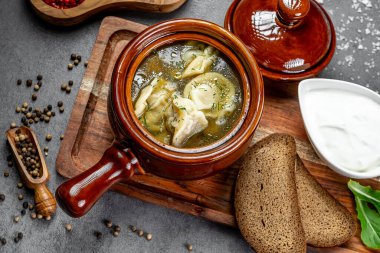 Köy kabında servis edilen lezzetli güveç. Hamur köftesiyle pişirilmiş doyurucu bir yahni, seramik bir kasede sunulmuş ekmek ve ekşi krema, ahşap tepside..