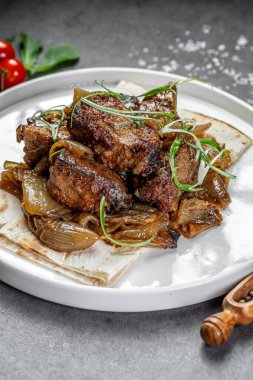 Soğanlı sığır eti ve kızarmış ekmek. Nefis biftek parçaları, karamelli soğanla kaplanmış, tabakta taze otlarla servis edilmiş..