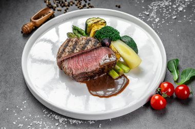 Sebzeli ve soslu gurme biftek. Beyaz tabakta taze sebzelerin yanında ızgara biftek nefis bir yemek deneyimi yaratır..