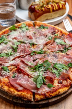 Tasty ham and herb pizza. A freshly baked pizza with ham and herbs sits on a wooden table, ready to be enjoyed with a refreshing drink.