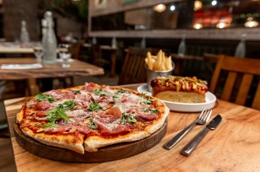 Pizza ve patates kızartması masada. Etli ve yeşillikli yeni yapılmış bir pizza ve sıcacık bir restoranda bir tabak patates kızartması..