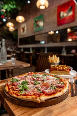 Pizza ve patates kızartması için rahat bir yer. Et ve yeşilliklerle kaplı taze bir pizza, sıcak bir yemek atmosferinde patates kızartmalarıyla birlikte ahşap bir tabakta oturur..