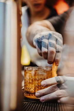 New York, ABD, 8 Temmuz 2025: Barmen bir barda kokteyl hazırlıyor. Karmaşık dövmeleri olan bir barmen barda portakal dilimiyle kokteyl süslüyor..
