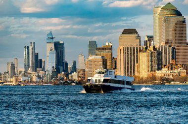 Hudson 'da feribotu olan Manhattan limanı. Bir feribot Hudson Nehri 'ni geçiyor. Arkasında Manhattan silueti olan açık bir gökyüzünün altında..