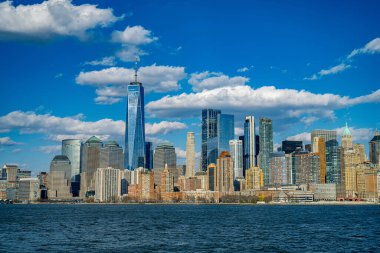 Nehrin üzerinde gökdelenler olan Manhattan gökdelenleri. Manhattan 'da parlak bir gün, New York' un özünü yansıtan bulutlar ve nehir önlerinde çarpıcı bir ufuk çizgisi gösteriyor..