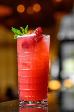 Cocktail with red juice and ice cubes. Glass of red cocktail with ice and mint on blurred background.