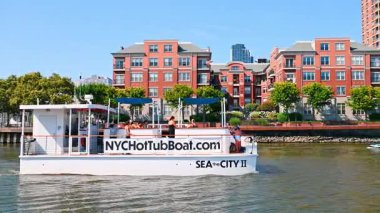 Turist teknesi SEA... Jersey Şehri nehir kıyısında yelken açıyor. Turist jakuzi teknesi SEA şehir, arka planda modern binalarla Jersey 'nin nehir kıyısında geziniyor..