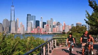 Jersey City gezinti güvertesinde Manhattan ufuk çizgisi manzaralı bir bisikletçi. Arka planda Manhattan silueti olan Jersey şehri boyunca bir bisikletçi geziniyor..