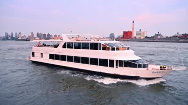 Yolcu feribotu New York 'ta East River' dan kalkıyor. Beyaz yolcu feribotu New York 'ta East River boyunca arka planda gökdelenlerle birlikte yol alır..