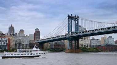 New York 'ta Manhattan Köprüsü' nün altından geçen bir yolcu gemisi. Beyaz bir yolcu gemisi Manhattan Köprüsü ve New York şehrinin arka planında şehir silueti olan Doğu Nehri boyunca yol alır..