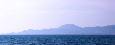 Sabahları kayalık bir adanın silueti sisli, şafakta sakin bir deniz.