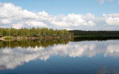 Orman gölü manzarası, bir gölün pürüzsüz yüzeyi, yansıyan bulutlar, parlayan bir orman gölü.