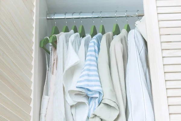 Summer wardrobe with linnen clothes on green hangers — Stock Photo, Image