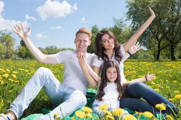 幸福的微笑家庭的父母和女孩与蒲公英花的草地上坐在阳光灿烂的夏天一天的肖像 — 图库照片