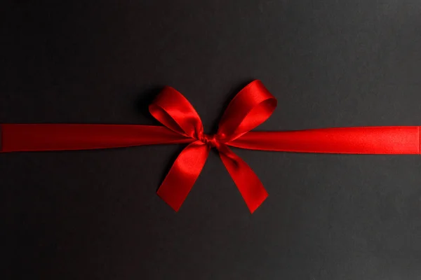 Shiny red satin ribbon and bow on black background. Holiday gift concept