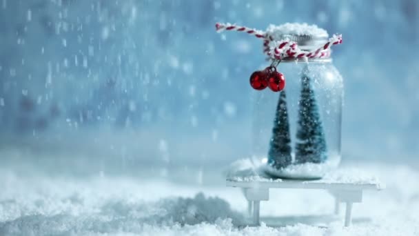 圣诞饰品的玻璃罐与条纹丝带 铃铛和冷杉树里面和落雪在蓝色背景 — 图库视频影像