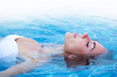 Girl in bikini relaxing floating in blue water of swimming pool clipart