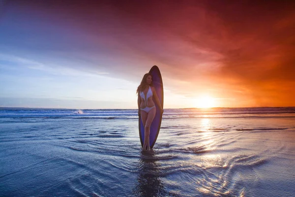 Surfer vrouw op het strand bij zonsondergang — Stockfoto